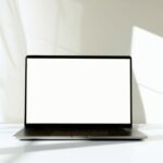 Magic Screen MacBook : le tactile à 139 dollars au CES 2026, mais le couvercle bloque A minimalist laptop with a blank screen on a white table, bathed in natural sunlight.