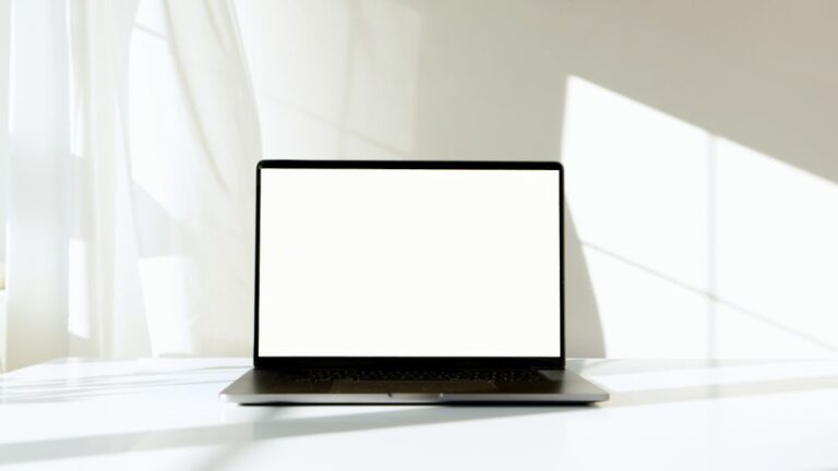 Magic Screen MacBook : le tactile à 139 dollars au CES 2026, mais le couvercle bloque A minimalist laptop with a blank screen on a white table, bathed in natural sunlight.