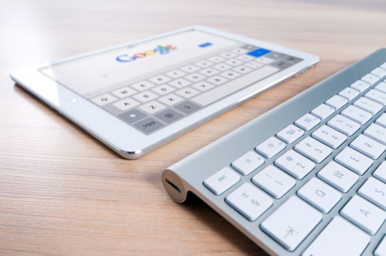 iPad : le 27 janvier 2010, l’ardoise sort du cartable A modern tablet displaying a search engine logo next to a wireless keyboard on a wooden desk.