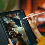 A person editing photos on a tablet with a stylus by a cozy fireplace setting.