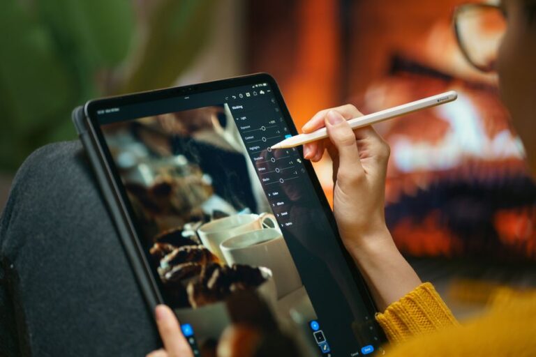 Pixelmator Pro arrive sur iPad le 28 janvier 2026, mais le pinceau a un péage A person editing photos on a tablet with a stylus by a cozy fireplace setting.