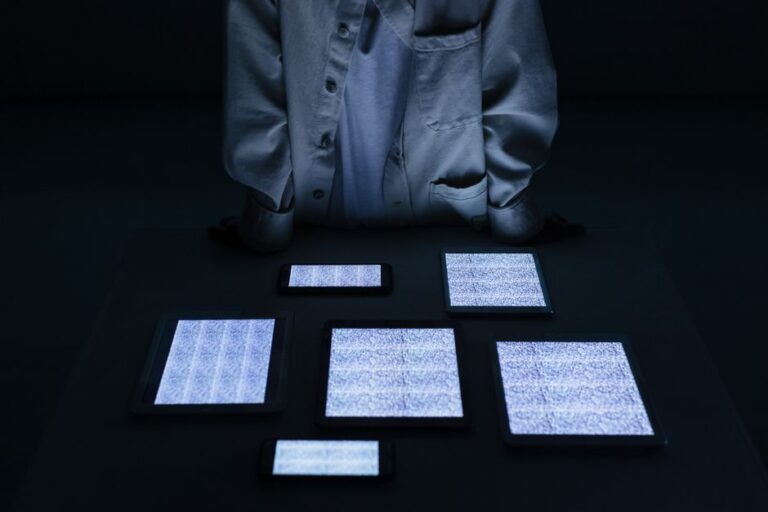 Tim Cook à la soirée Melania, le 24 janvier 2026 : la photo qui coûte cher A person in a white shirt stands over tablets and phones with static screens in a dark room.