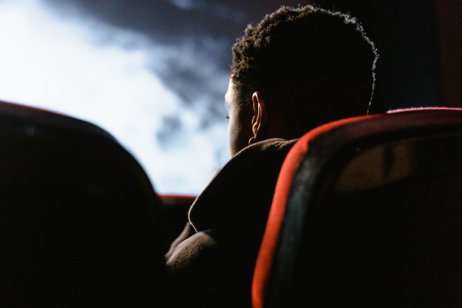 A person sits in a theater watching a movie on a large screen, enveloped in a dark ambiance.