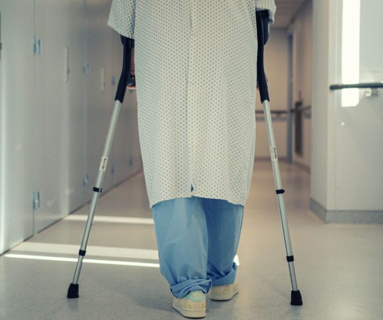 Apple Health après fracture de la cheville : les pas reviennent, la vitesse reste en retrait à 12 mois A senior patient using crutches to walk down a hospital corridor, symbolizing recovery and mobility assistance.