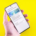 iOS 26.3 bêta 3 arrive le 26 janvier : Apple serre les boulons A smartphone displaying an update notification held by a person's hand against a bright yellow background.