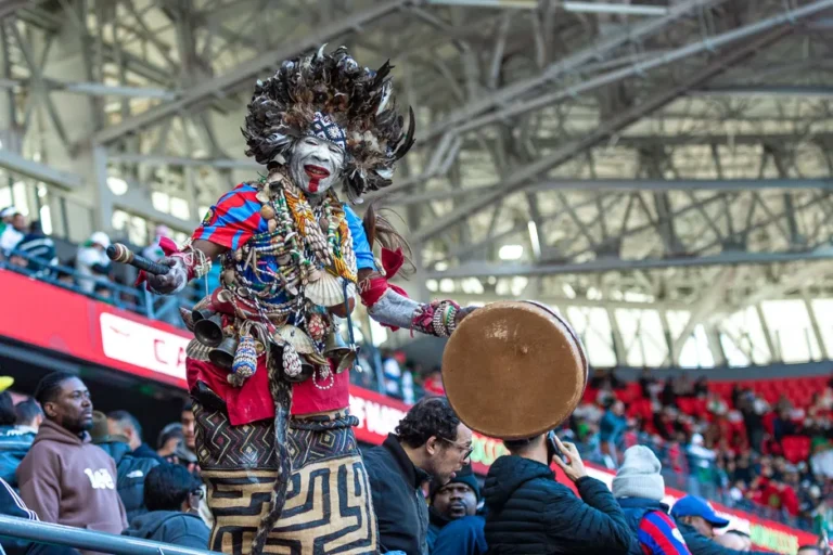 Bad Bunny au Super Bowl LX: 13 minutes de show, La Casita et politique A vibrant traditional performer with feathers and drum at a lively public event indoors.