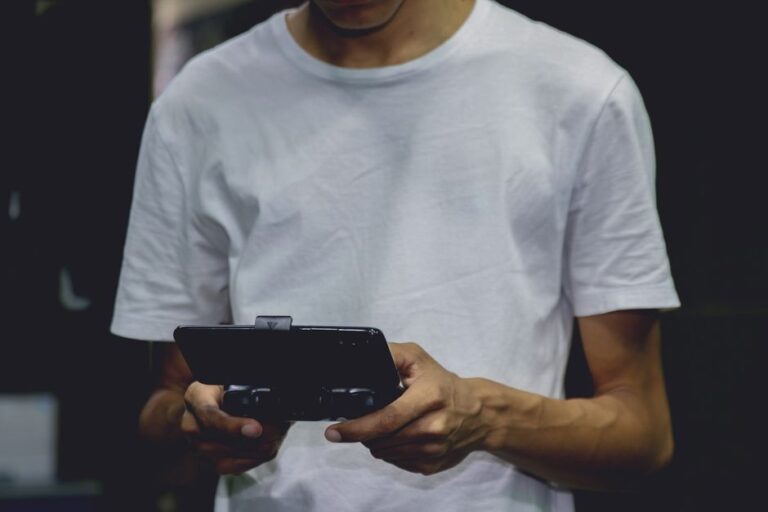 8BitDo FlipPad : la manette portrait attend l’été 2026 A young man in a white shirt using a smartphone game controller indoors.