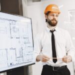 L'Air de rien, le designer de l'iPhone Air rejoint Hark en 2025 Architect in orange helmet presenting building blueprints in a modern office setting. Professional and confident.