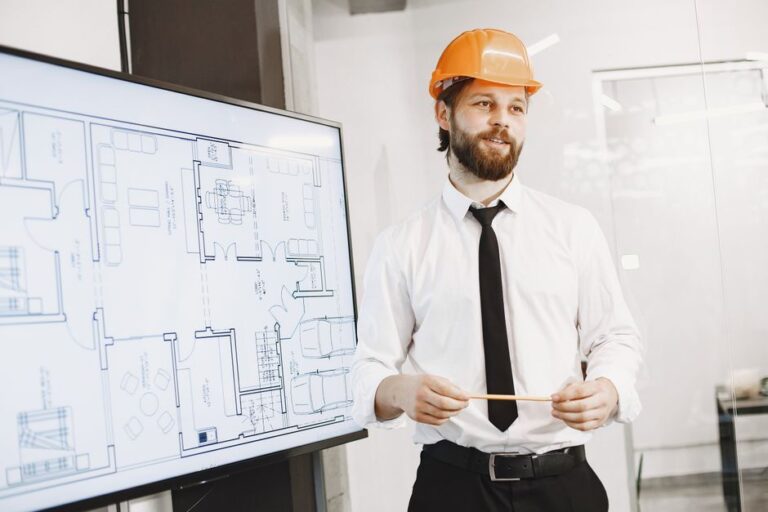 L’Air de rien, le designer de l’iPhone Air rejoint Hark en 2025 Architect in orange helmet presenting building blueprints in a modern office setting. Professional and confident.