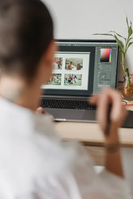 Back view of crop anonymous graphic designer with short hair in white shirt working on laptop using touchpad while retouching photos