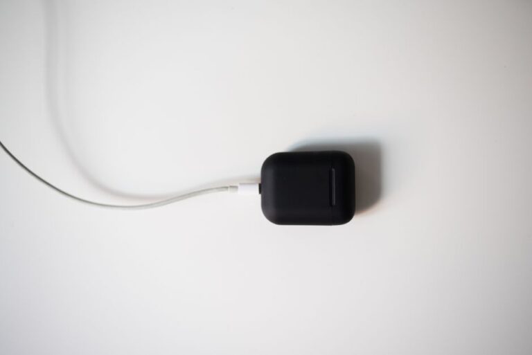 Black earbud case with charging cable on white background in minimalist style.