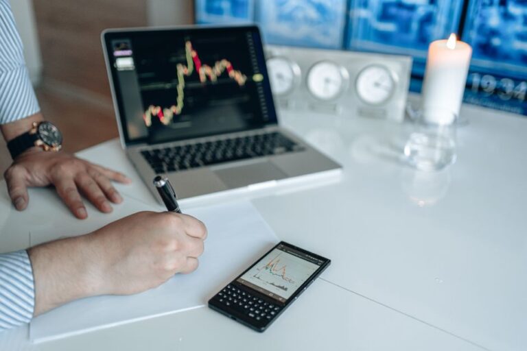 Apple à 330 dollars : l’iPhone 17 convainc Evercore, la RAM veille Business analyst writing with laptop and smartphone showing trend graphs on a white desk.