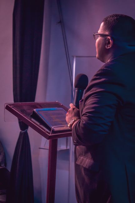 Business professional speaking at a podium with a microphone and tablet inside a venue.