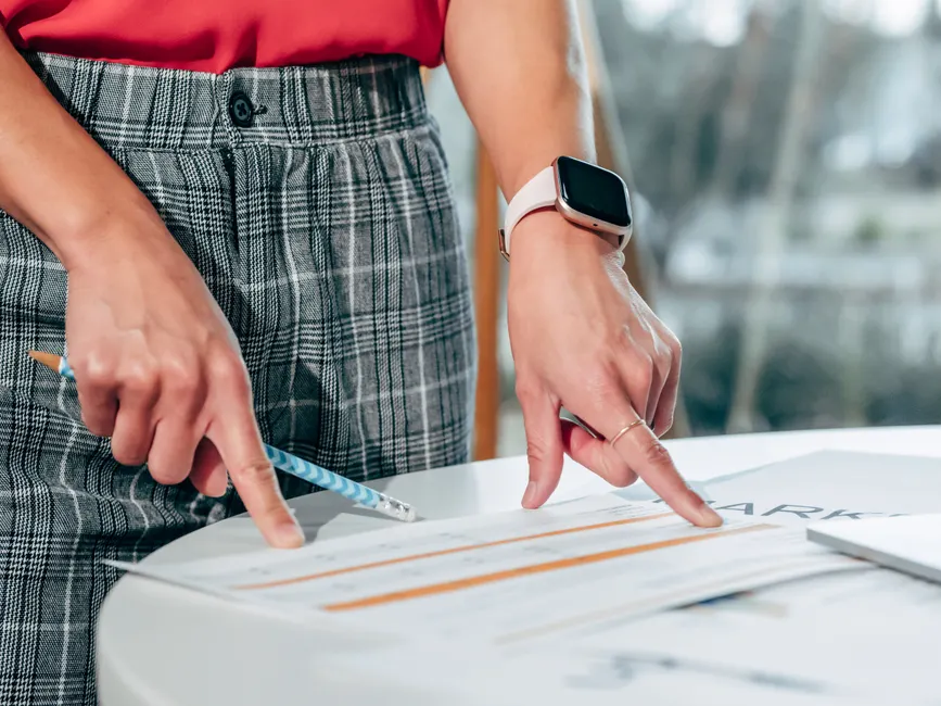 Businesswoman examining documents on a desk with a smartwatch and pen.