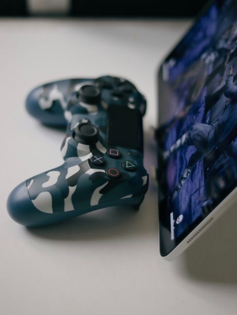 Close-up of a camouflage game controller next to a tablet displaying a game screen.
