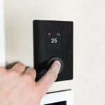 Eve Thermostat à 129,95 dollars : Matter entrouvre le jardin clos Close-up of a hand adjusting a sleek, modern smart thermostat on a wall.