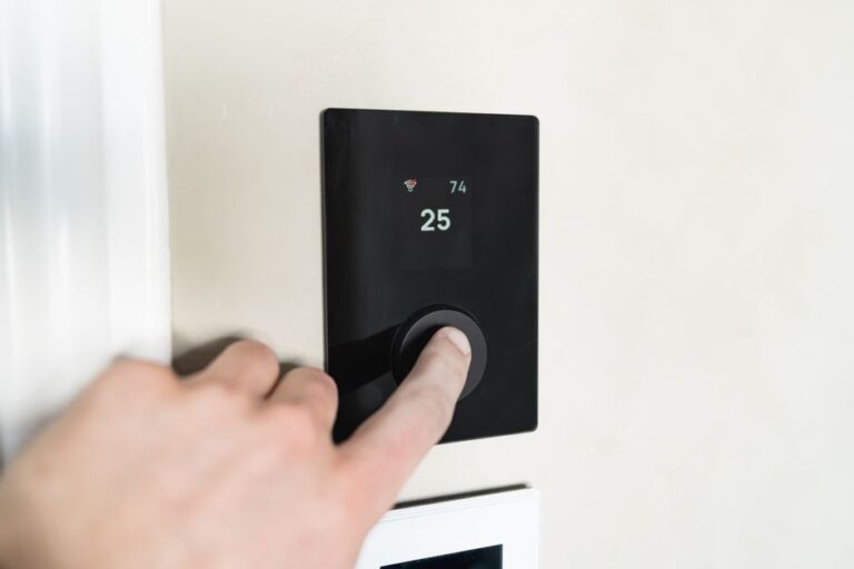 Close-up of a hand adjusting a sleek, modern smart thermostat on a wall.