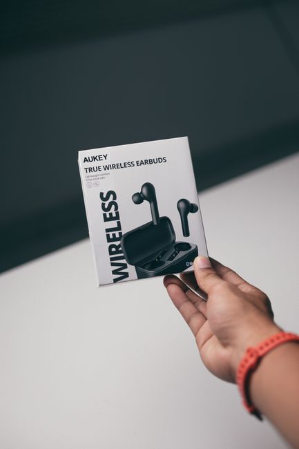 Close-up of a hand holding a box of Aukey true wireless earbuds, highlighting sleek design.