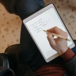 Close-up of a person writing on a tablet with a stylus in a cozy indoor environment.