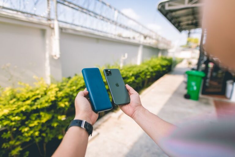 Close-up of a smartphone and power bank held in hands in an outdoor setting.