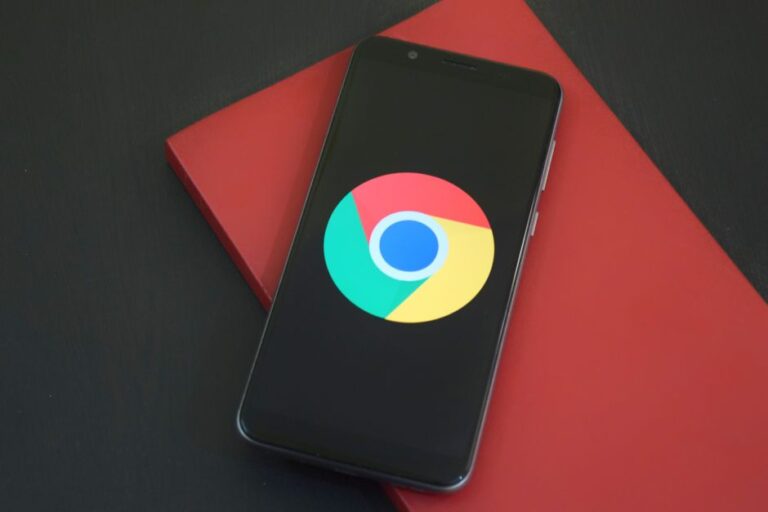 Adoption d’iOS 26 : le piège des 16,3 % Close-up of a smartphone with Chrome browser logo on screen placed on a red notebook.