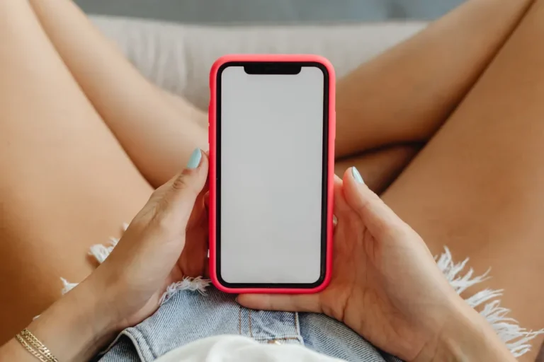 iPhone 17 : 111,2 milliards pour Apple en mars 2026, le futur trinque Close-up of a woman holding a smartphone in denim shorts, showcasing the phone display.