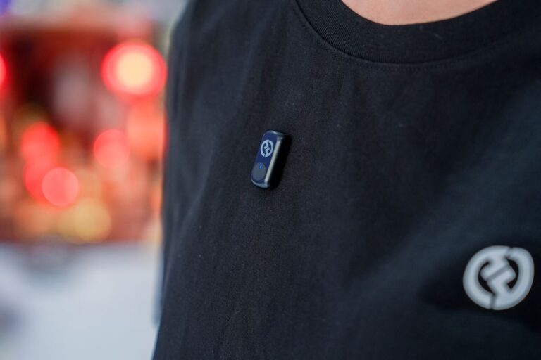 Apple préparerait un pin AI en 2027 : 20 millions visés Close-up view of a wearable tech device clipped on a black t-shirt against a blurry background.