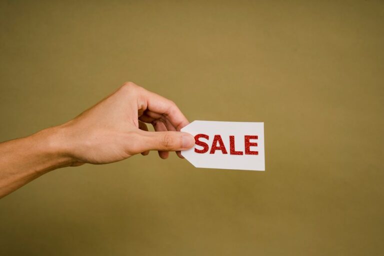 AirPods et Beats dès 99 dollars le 4 janvier 2026 : la promo ne dit pas tout Crop anonymous person showing small white paper tag with inscription Sale against brown wall