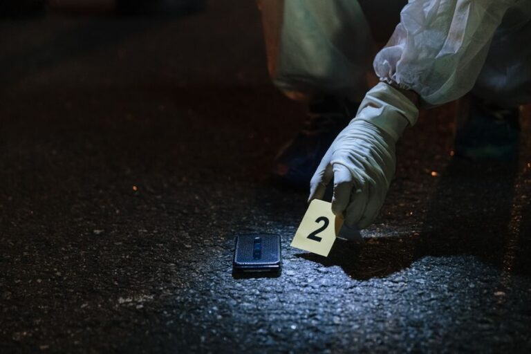 Vols d’iPhone autour de janvier 2026 : AirTag, braquages et pièges Apple Forensic investigator examining evidence in a city street at night.