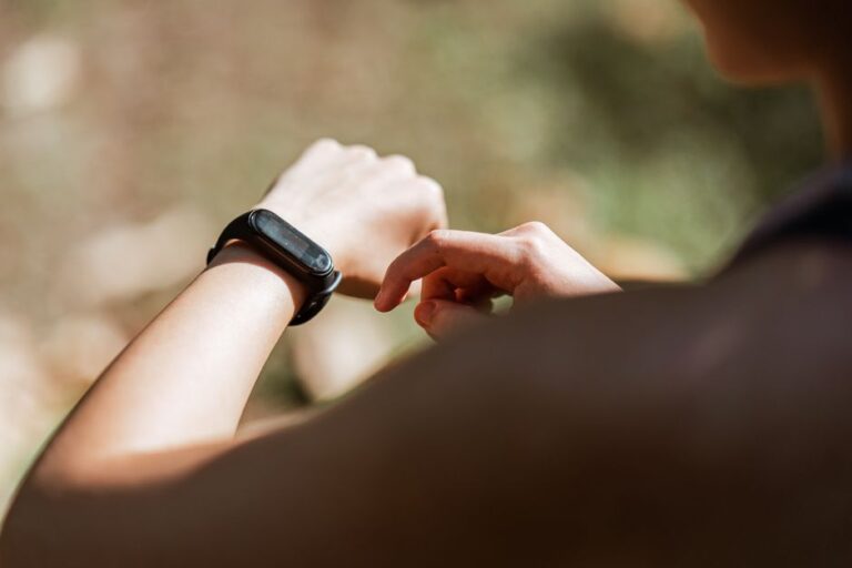 From behind crop anonymous sportswoman checking notifications on modern fitness tracker while training against blurred nature background on sunny weather