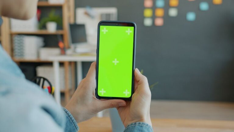 Grok bloque les faux nus le 15 janvier 2026, Apple sous pression Hands holding a smartphone with green screen in a modern office setting.