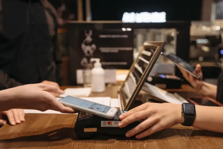 Apple Pay en Australie : la CBA veut négocier le péage NFC en 2026 Hands using mobile for contactless payment at café terminal.