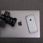 High-angle shot of DSLR camera, MacBook, and iPhone on textured surface, showcasing modern technology essentials.