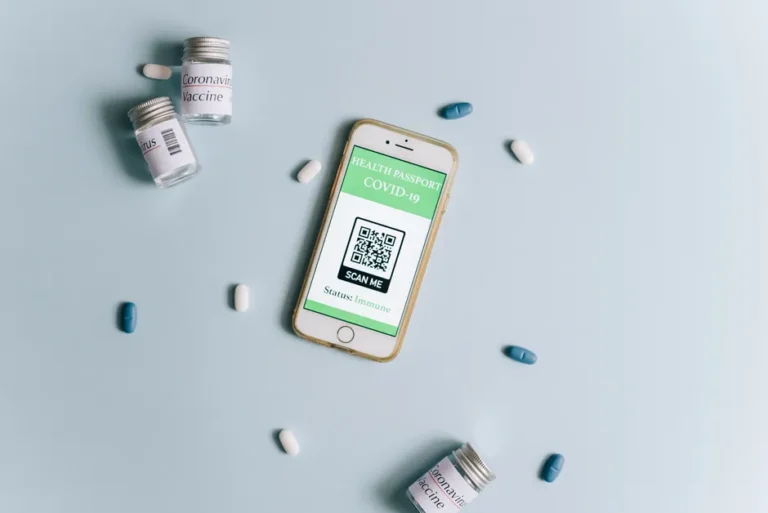 iPhone 18 Pro attendu en septembre 2026 : la Dynamic Island rétrécirait Image of a smartphone displaying a health passport alongside COVID-19 vaccine vials and pills on a light blue background.