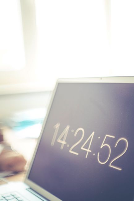 Laptop screen showing digital clock with blurred bright office background.