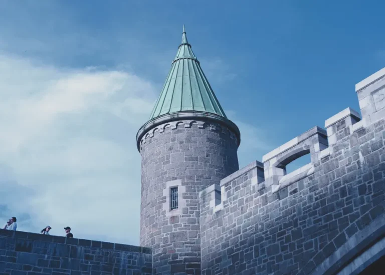 Low angle view of a historic castle tower and walls under a blue sky.
