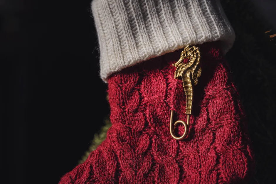 Luxurious golden seahorse pin adorns a red knitted sock, adding charm against a black background.