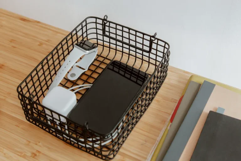 CES 2026 : Pepcom coupe une batterie de 10 000 mAh en deux Organized workspace with tech gadgets in a wire basket on a wooden desk.