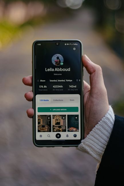 Person holding smartphone displaying user profile, outdoors with bokeh background.