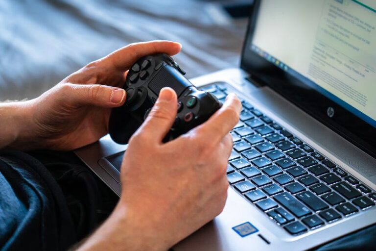 Apple M4 sur Steam à 19,60 % : le M5 attend son tour Person holds a gaming controller while interacting with a laptop, emphasizing modern gaming technology.