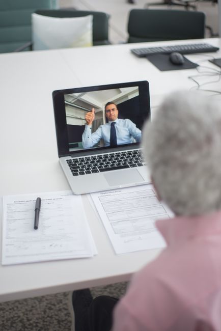 Senior man engages in a video conference with a colleague on a laptop, discussing documents.