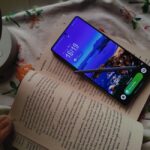 Smartphone displaying a scenic beach wallpaper atop an open book, illuminated by soft daylight.