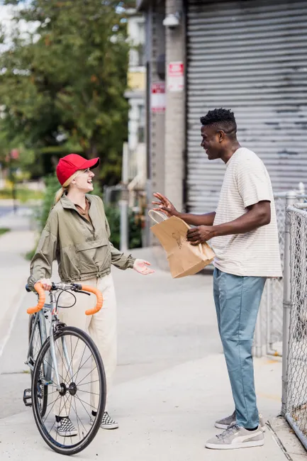 Smiling courier hands off package to client on urban street with bike.