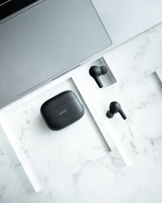Top view of sleek wireless earbuds and case on a marble surface next to a laptop.