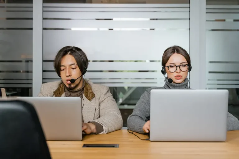 Fausses pubs Mac : le faux support Apple passe par Terminal Two employees at a call center working with laptops and headsets, focused on customer support.