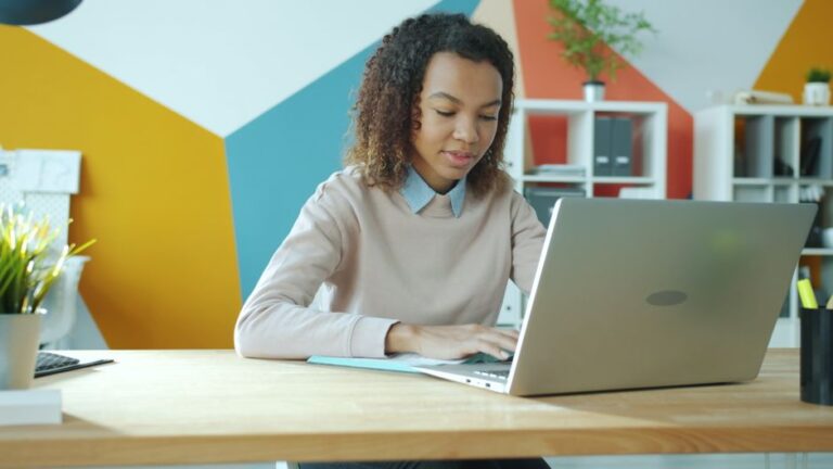 Apple teste Enchante et Enterprise Assistant en 2026 : Siri attend encore Young woman focused on work at a modern office, using laptop. Bright and vibrant setting.